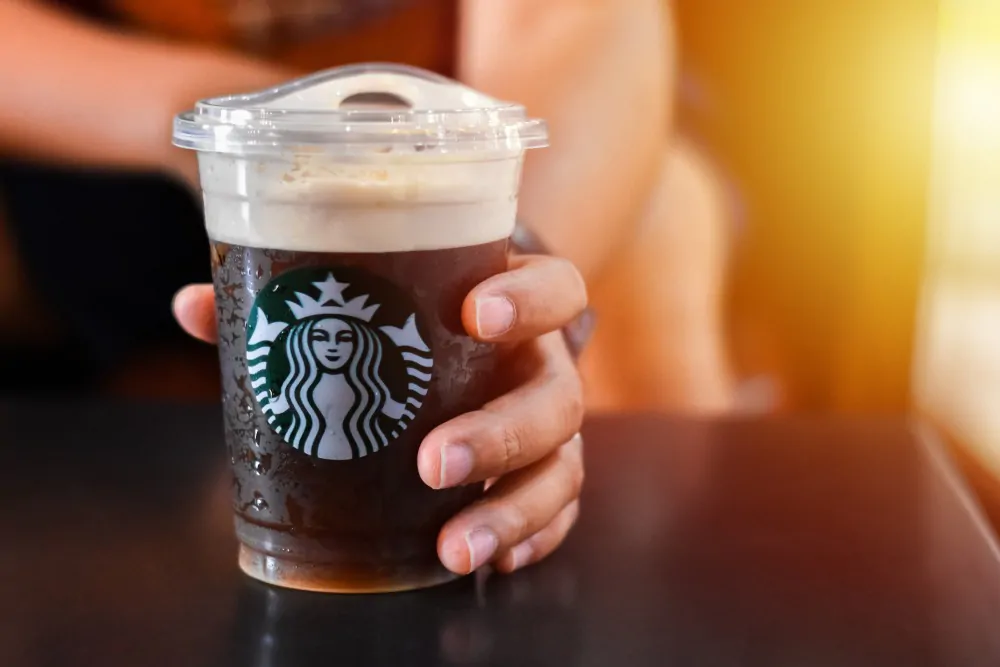 Man holding a Starbucks cold brew beverage cup in hand. Starbucks is the world's largest coffee house with over 20,000 stores in 61 countries.