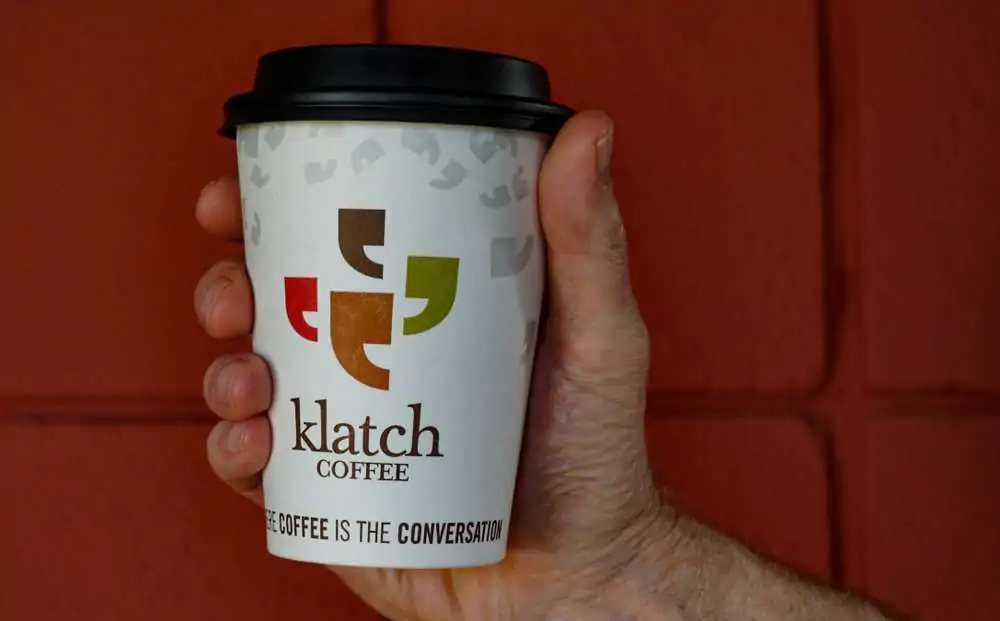 Customer holds a cup of coffee to go from Klatch, a local family business that has been serving award winning coffee for 25 years