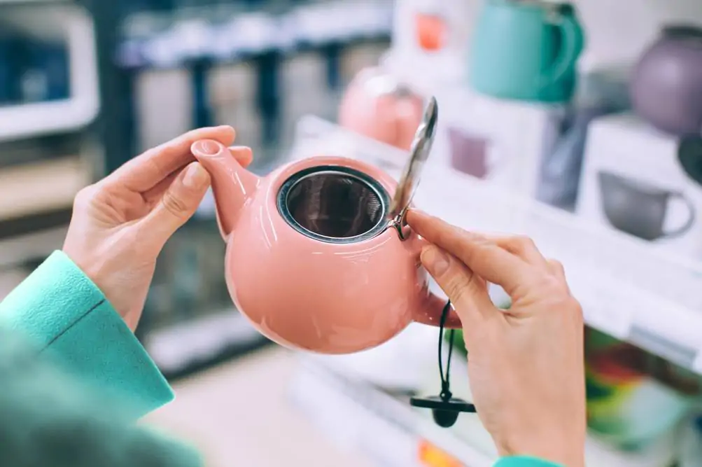 Pink teapot in the hands of a girl on the background of a supermarket counter
